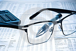 Glasses near calculator with pen on financial newspaper
