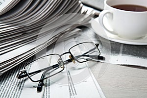Glasses on newspapers and a cup of coffee on the table