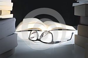 Glasses and open book on table surrounded by literature.