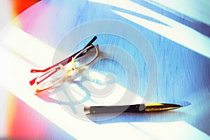 Glasses and pen lie on a white wooden table in the morning sun. The sun`s glare. Toned. Copy of the space.