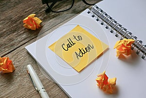 Glasses,pen,trash paper notebook and yellow sticky note written with Call to Action on wooden background