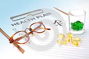 Glasses and pill capsules on health plan notes
