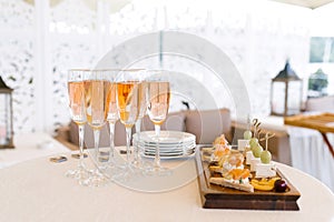 Glasses of pink champagne stand on the buffet table next to a plate of appetizers