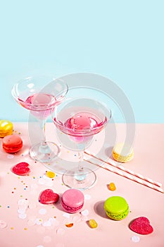 Glasses of pink cocktails with heart candies and macaroons on pink table. Birthday party or Valentines day concept