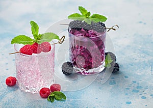 Glasses of pink soda lemonade and blackberry cocktail with ice cubes and mint on light blue background