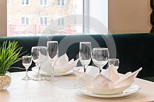 Glasses, plates, napkins served for dinner in restaurant with cozy interior