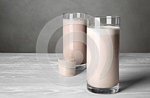 Glasses with protein shake and scoop of powder on white wooden table.