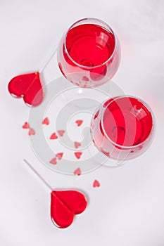 Glasses of red grape wine with red candies heart shape on the white background. Top view