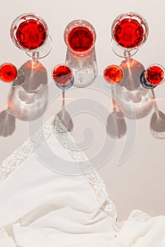 Glasses with red juice or wine on pastel beige background with shades and white cloth. Summer drinks and refreshment concept.