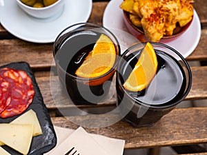 Glasses of red vermouth served with orange and Spanish tapas