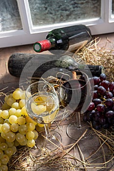 Glasses of red and white wine with grape, bottles at background