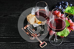 Glasses of red wine, bottle opener and ripe grapes on dark wooden table