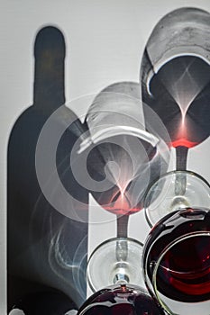 Glasses of red wine and bottle with shadows and reflections on a white textured surface.