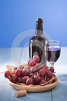 Glasses of red wine with red grapes and a bottle of wine on blue