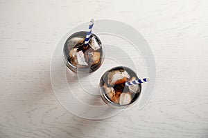 Glasses of refreshing cola with ice cubes and straws on white wooden background