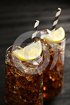 Glasses of refreshing soda water with ice cubes and lemon slices on black table, closeup