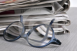 Glasses resting next to a stack of newspapers