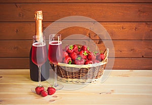 Glasses of rose champagne, bottle of rose champagne and fresh strawberry in wicker basket on wooden table near wooden wall