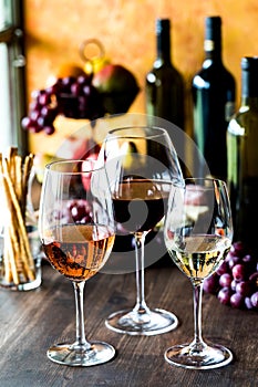 Glasses of rose, red and white wine with wine bottles and fruit in behind.