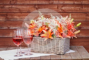 Glasses of rose wine and wicker basket with orange lilies and white astilbe flowers