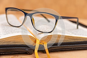 Glasses for sight lie on the Bible, the Bible in leather black cover with tabs lies on the table