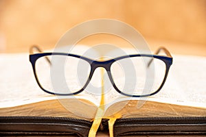 Glasses for sight lie on the Bible, the Bible in leather black cover with tabs lies on the table