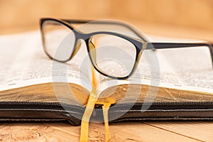 Glasses for sight lie on the Bible, the Bible in leather black cover with tabs lies on the table