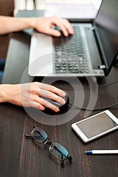 Glasses and smartphone on the table, laptop with human hands on a background