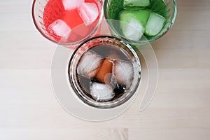 Glasses of soft drink with ice cubes and bubbles on wooden table