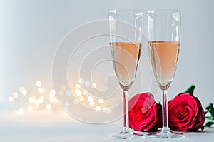 Glasses of sparkling Rose wine with red roses on white background