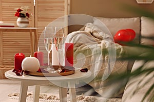 Glasses of sparkling wine, candles and petals on white table indoors. happy Valentine`s Day