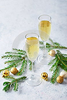 Glasses with sparkling wine type champagne with fir branches and golden Christmas tree decorations on light background