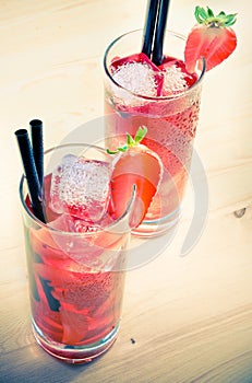 Glasses of strawberry cocktail with ice on old wood table, old style