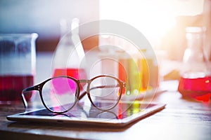 Glasses on tablet screen with blurred science equipments on back