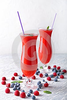 Glasses of tasty red smoothie and berries on light table