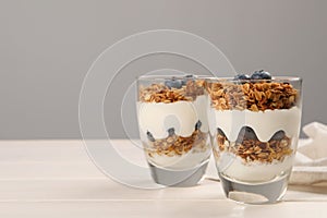 Glasses of tasty yogurt with muesli and blueberries served on white wooden table, space for text