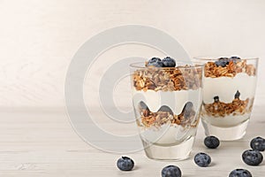 Glasses of tasty yogurt with muesli and blueberries served on white wooden table, space for text