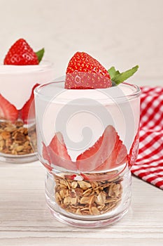 Glasses of tasty yogurt with muesli and strawberries served on white wooden table