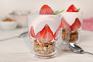 Glasses of tasty yogurt with muesli and strawberries served on white wooden table