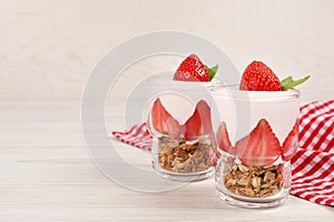 Glasses of tasty yogurt with muesli and strawberries served on white wooden table, space for text