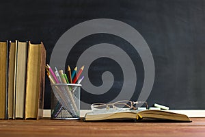 Glasses teacher books and a stand with pencils on the table, on the background of a blackboard with chalk. The concept of the teac