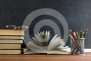 Glasses teacher books and a stand with pencils on the table, on the background of a blackboard with chalk. The concept of the teac