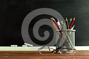 Glasses teacher and a stand with pencils on the table, on the background of a blackboard with chalk. The concept of the teacher`s