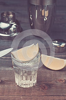 Glasses of tequila with a lime/preparation of shot with a lime in a shaker on a wooden background. Toned