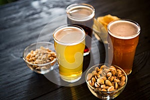Glasses with three different types of beer. Nuts, rusks and chips in bowls on wooden table