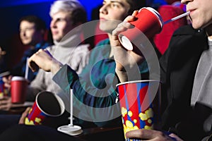 Glasses with a tube and popcorn in the hands of people in a movie theater close-up