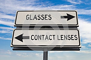 Glasses versus contact lenses road sign with two arrows on blue sky background. White two street sign with arrows on metal pole.