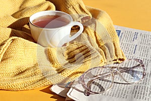 Glasses for vision with a cup of hot tea on a knitted sweater, a fresh newspaper, a side view-the concept of a cozy pastime for