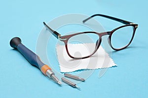 Glasses for vision, a lens cleaning cloth, and a screwdriver for repairs on a blue background. Glasses repair concept