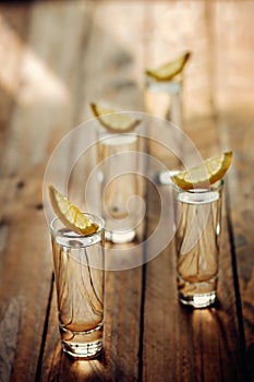 Glasses of vodka with lemon on wooden table. Toning image.